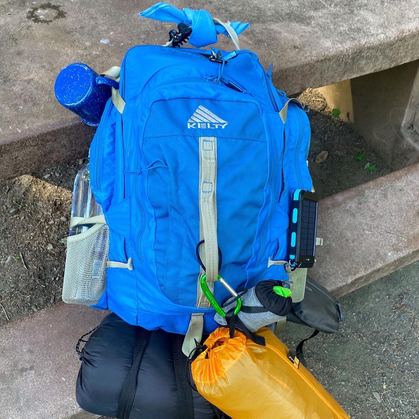 Backpack purchased second-hand with sleeping bag, camping mug, and sleeping pad attached to the outside and ready for a backpacking trip.